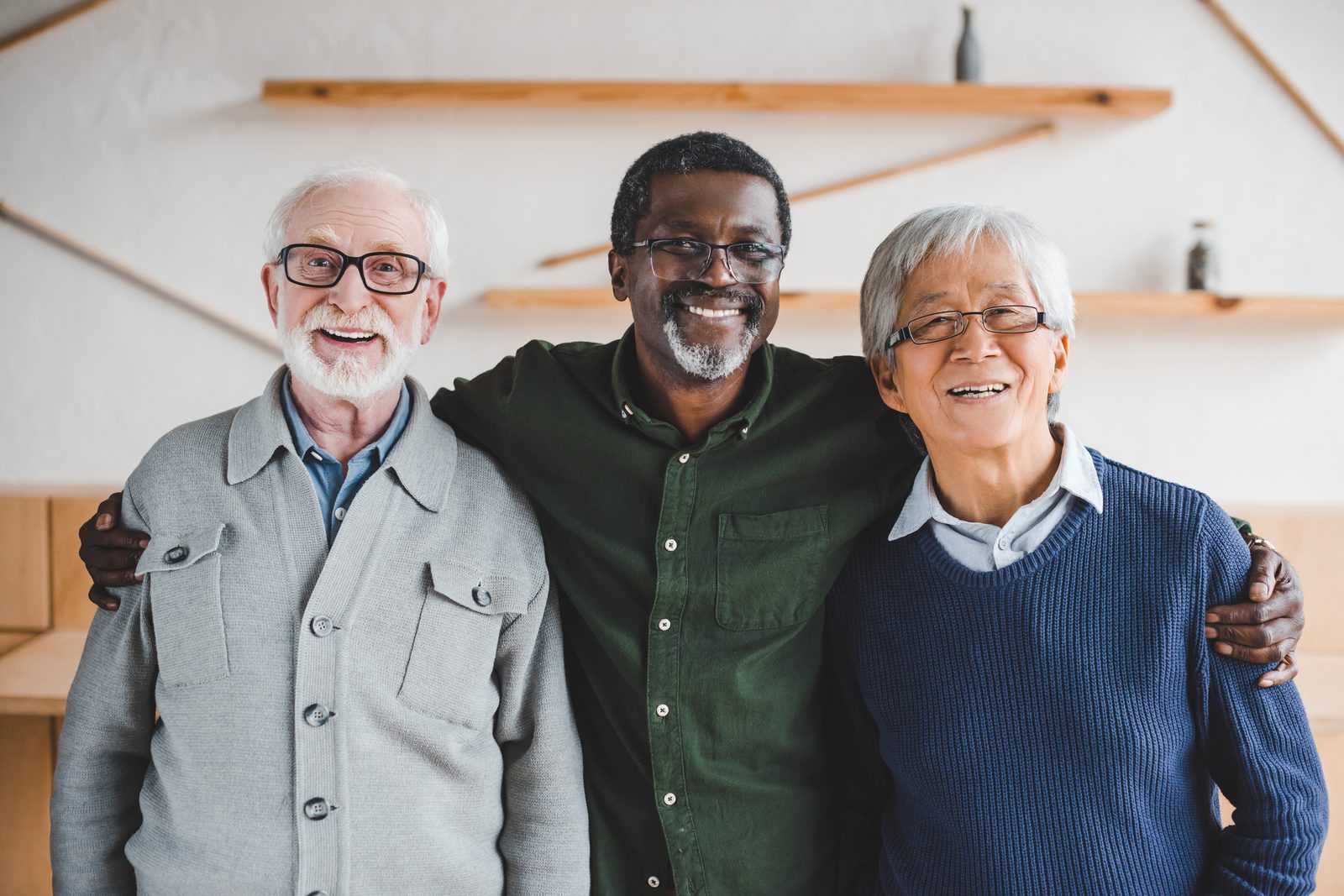 Three older men smiling and embracing together.